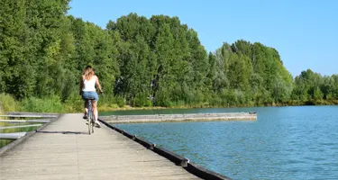 Une femme fait du vélo au bord du lac du parc naturel de passeligne, à Agen