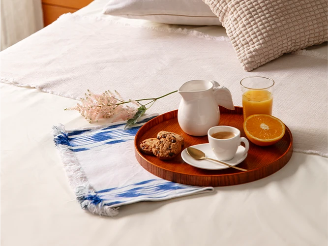 Un plateau de petit déjeuner est posé sur un lit, avec un jus d'orange, un café et des cookies